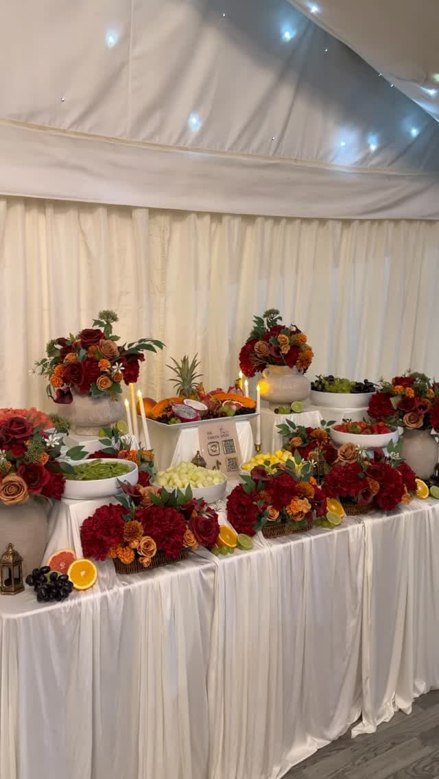 A fruit table arranged with florals, candles, and layered bowls.